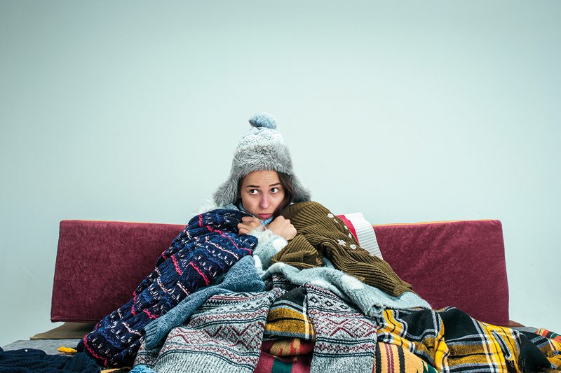 The young woman sitting on sofa at home or studio covered with knitted warm clothes. Relaxation at Home. 