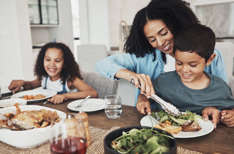 Mom, children and eating food in home together for lunch, dinner table and healthy meal. Happy family, mother and kids smile for dining in house with love, care and happiness of delicious supper.