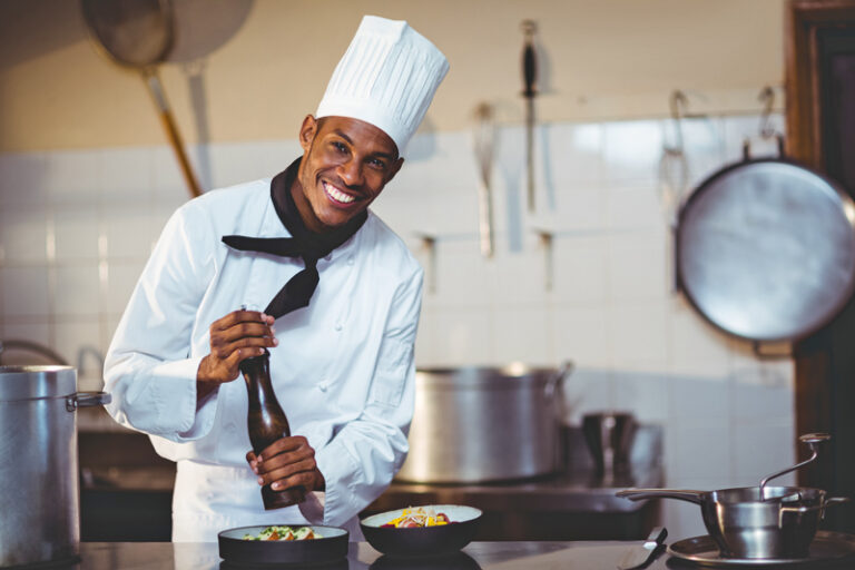 Portrait of chef sprinkling pepper on a meal in commercial kitchen