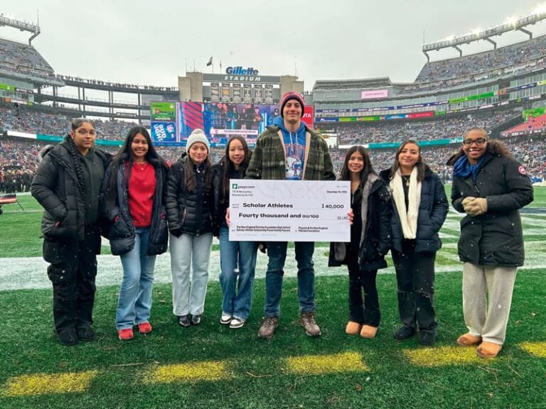 Representante de la Fundación New England Patriots entrega cheque a estudiantes favorecidos.