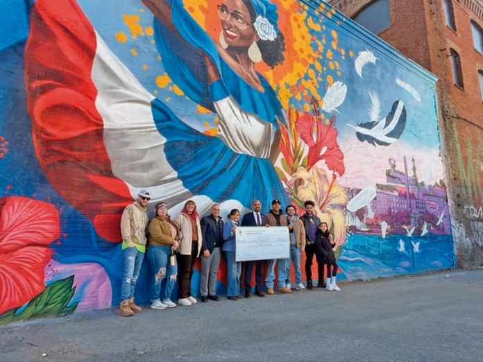 Ante uno de los gigantescos murales, el Senador Pavel Payano entrega cheque para expandir murales públicos en toda la ciudad.