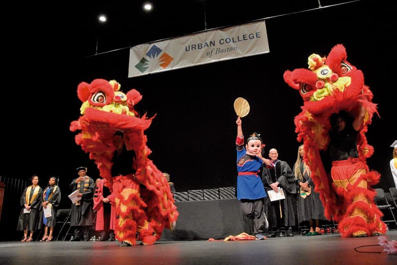Urban College of Boston celebra 30 años de logros académicos 3 Gund Kwok Asian Women’s Lion and Dragon Troupe open Urban College of Boston 2026 commencement ceremony with traditional lion dance performance.