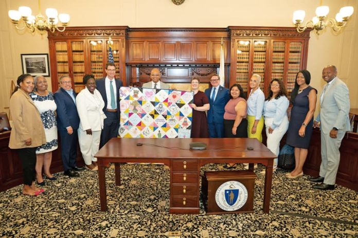 12-SaludMaterna_1 Speakers pose with a homemade quilt presented as a gift to Governor Healey: (from left to right) Mariah Sabir, Grounded MAMA; Mimi Gardner, NeighborHealth; Dr. Julio Mazul, NeighborHealth; Dr. Ndidiamaka Amutah-Onukagha, Tufts University; Jamie Hazard, NeighborHealth; Dr. Kiame Mahaniah, Massachusetts Executive Office of Health and Human Services; Emily Anesta, Bay State Birth Coalition; David Seltz, Massachusetts Health Policy Commission; Rosemary Raymundo, NeighborHealth; Nashira Baril, Neighborhood Birth Center; Cindy Cruz, Harbor COV; Dr. Bisola Ojikutu, Boston Public Health Commission; and Michael Curry, Massachusetts League of Community Health Centers.