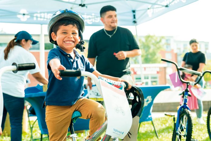 Un joven residente de Chelsea recibe con alegría su nueva bicicleta, donada por First Priority Credit Union para la rifa de bicicletas de NeighborHealth.